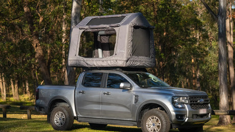 Ford Ranger centred in frame with the grey Often rooftop tent deployed on the roof rack, parked among eucalypts, showing the total height of the setup