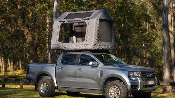 Ford Ranger centred in frame with the grey Often rooftop tent deployed on the roof rack, parked among eucalypts, showing the total height of the setup