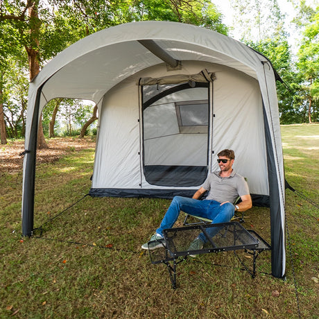 Camper resting on a stretcher under the Often Sunday canopy awning at a shaded grass campsite