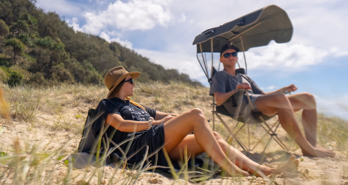 A couple reclining in Often camping chairs on a Queensland dune, one of them under the chair's own sun canopy.