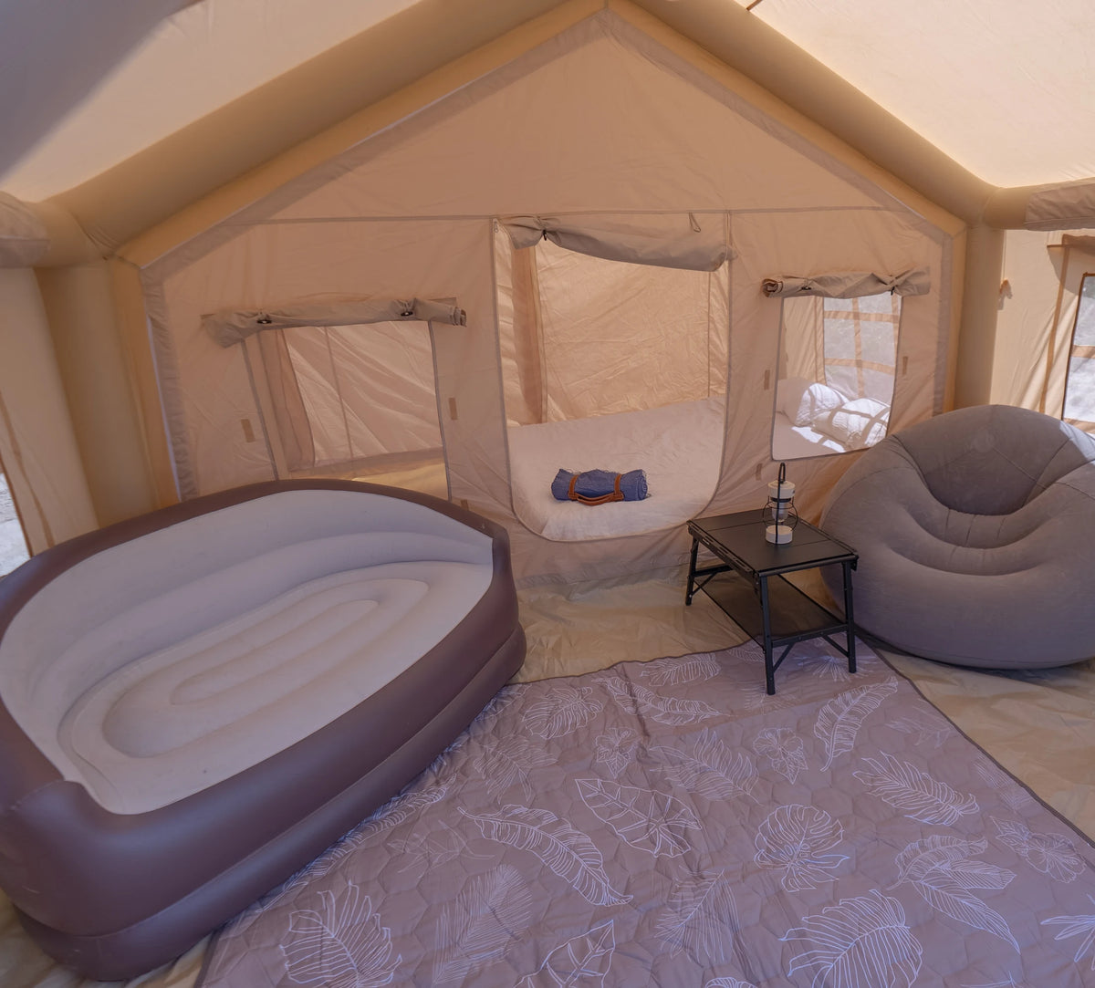 Inside an Often glamping tent furnished for the night: a double air bed, an inflatable armchair, a folding side table with a lantern on it and a mat over the floor.