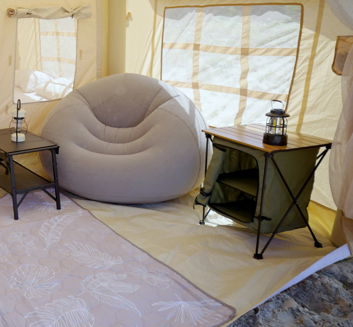 An Often folding table with its fabric storage cabinet open underneath, a lantern on the timber top and an inflatable armchair beside it inside a glamping tent.