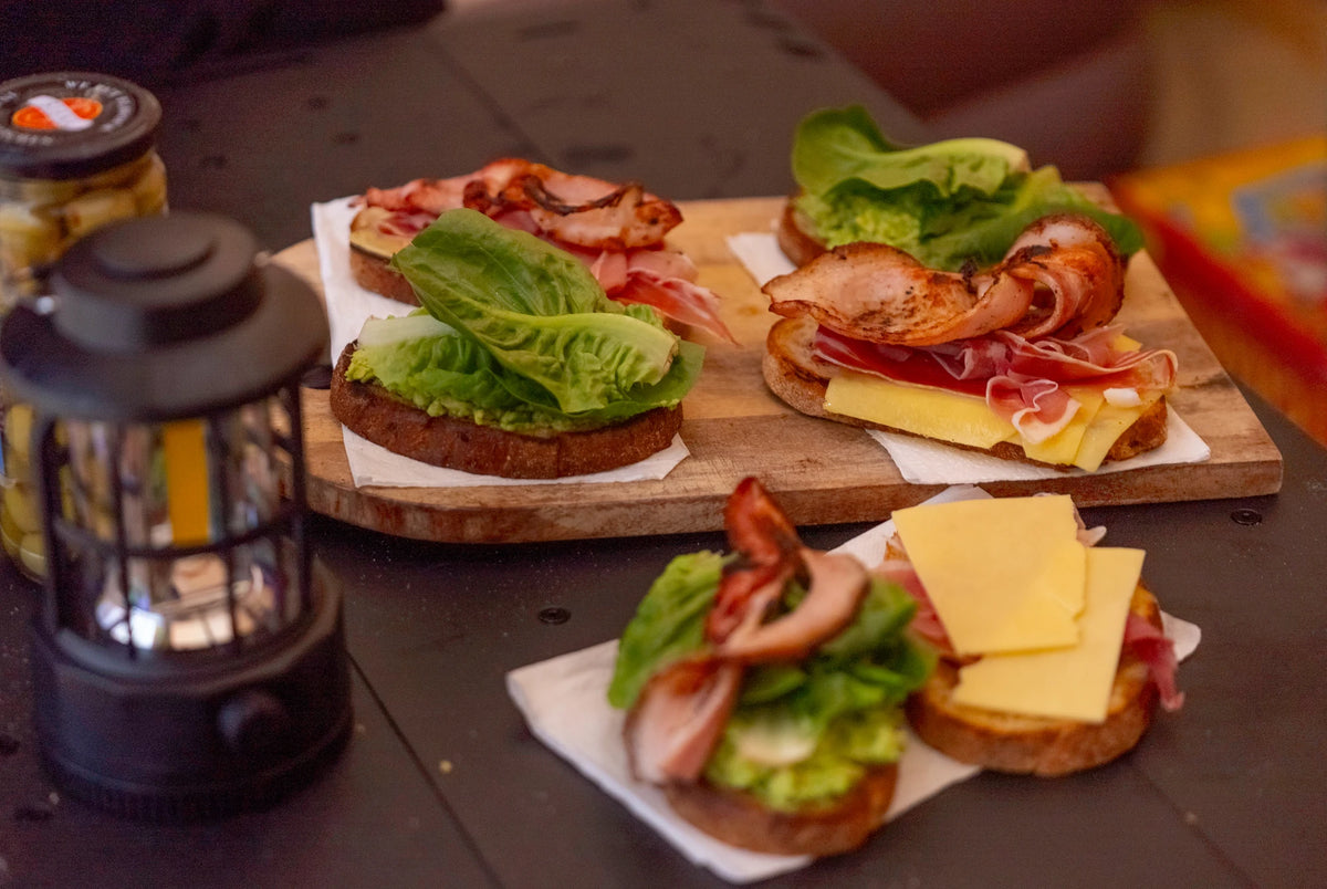 Breakfast laid out on a wooden board on an Often camp table, with a retro lantern standing beside it.