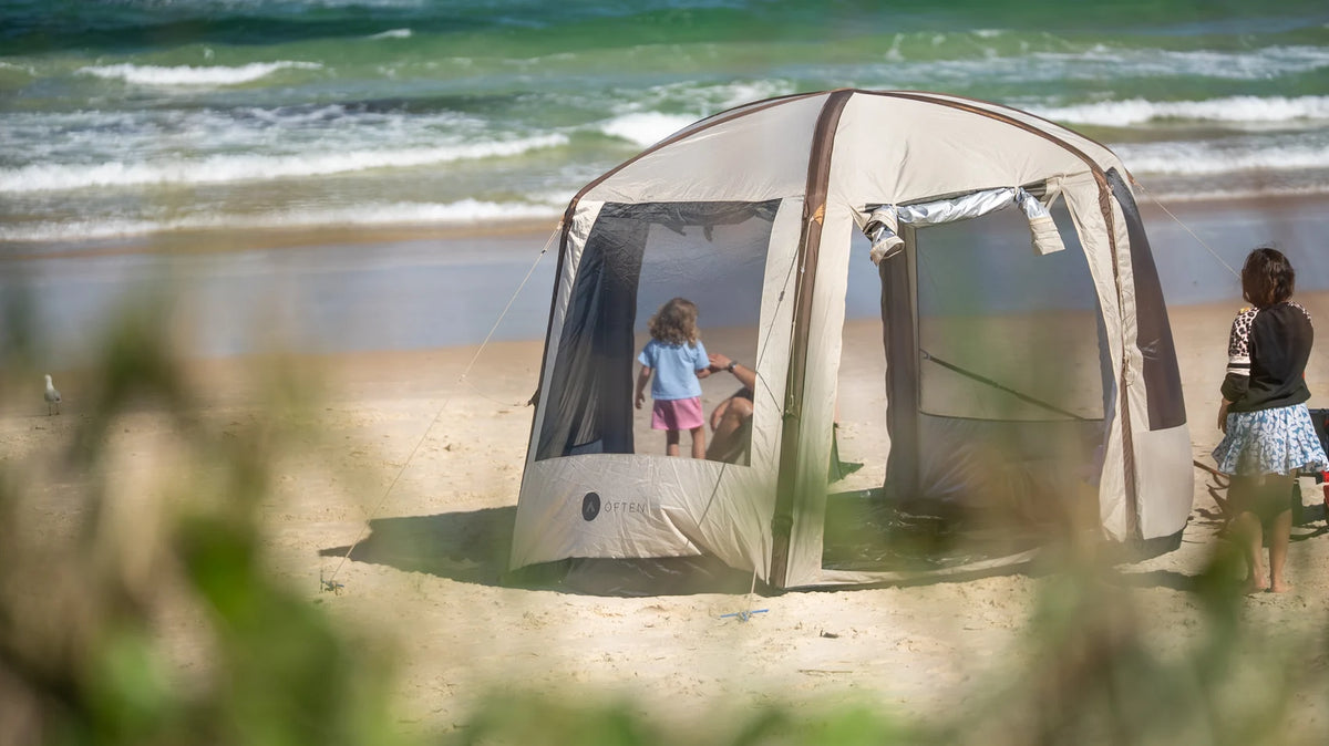 Children playing on the sand beside an Often inflatable glamping tent at the beach
