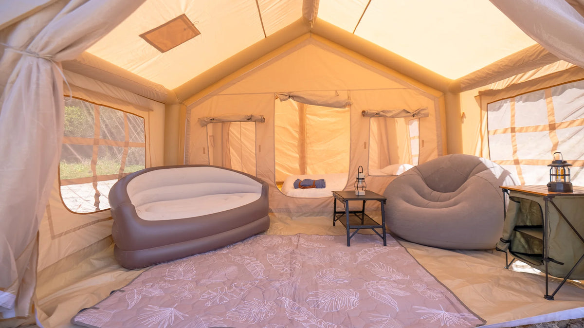 Inside an Often Glamp Series inflatable tent furnished with a double air bed, a grey inflatable armchair, a folding side table and a camping lantern