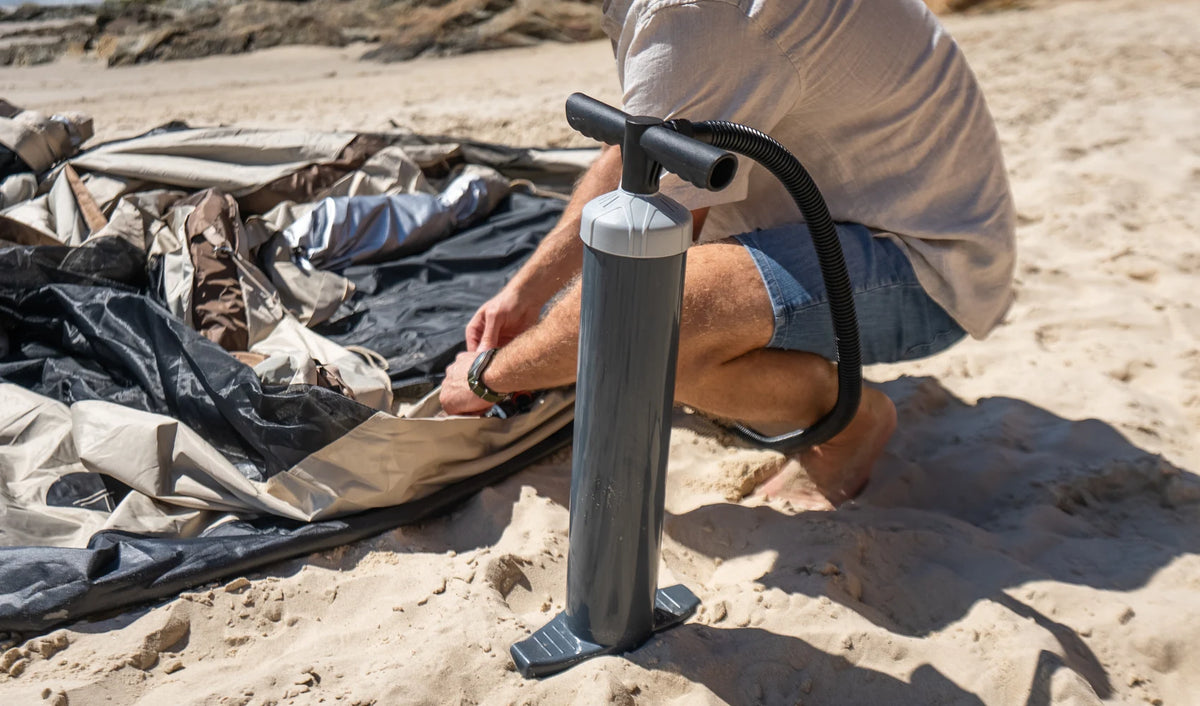 One person inflating an Often glamping tent on the sand with the included manual pump