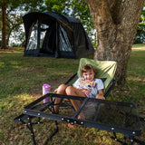 Child in a camp chair beside the Often Raven pitched on grass under a tree