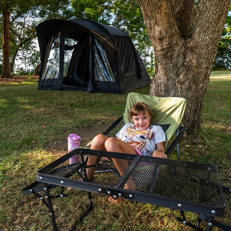 Child in a camp chair beside the Often Raven pitched on grass under a tree